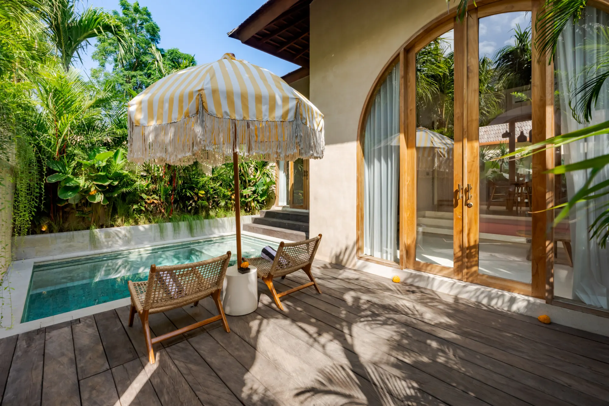 Striped umbrella seating area by pool with lush garden surrounds