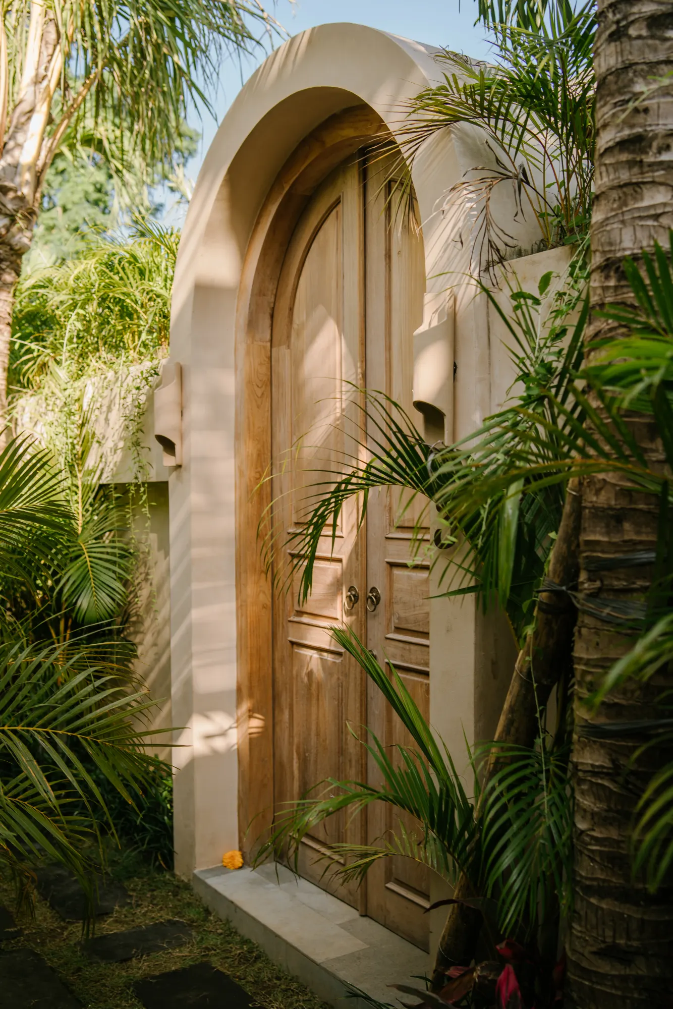 Sculptural wooden doorway surrounded by vibrant palm foliage