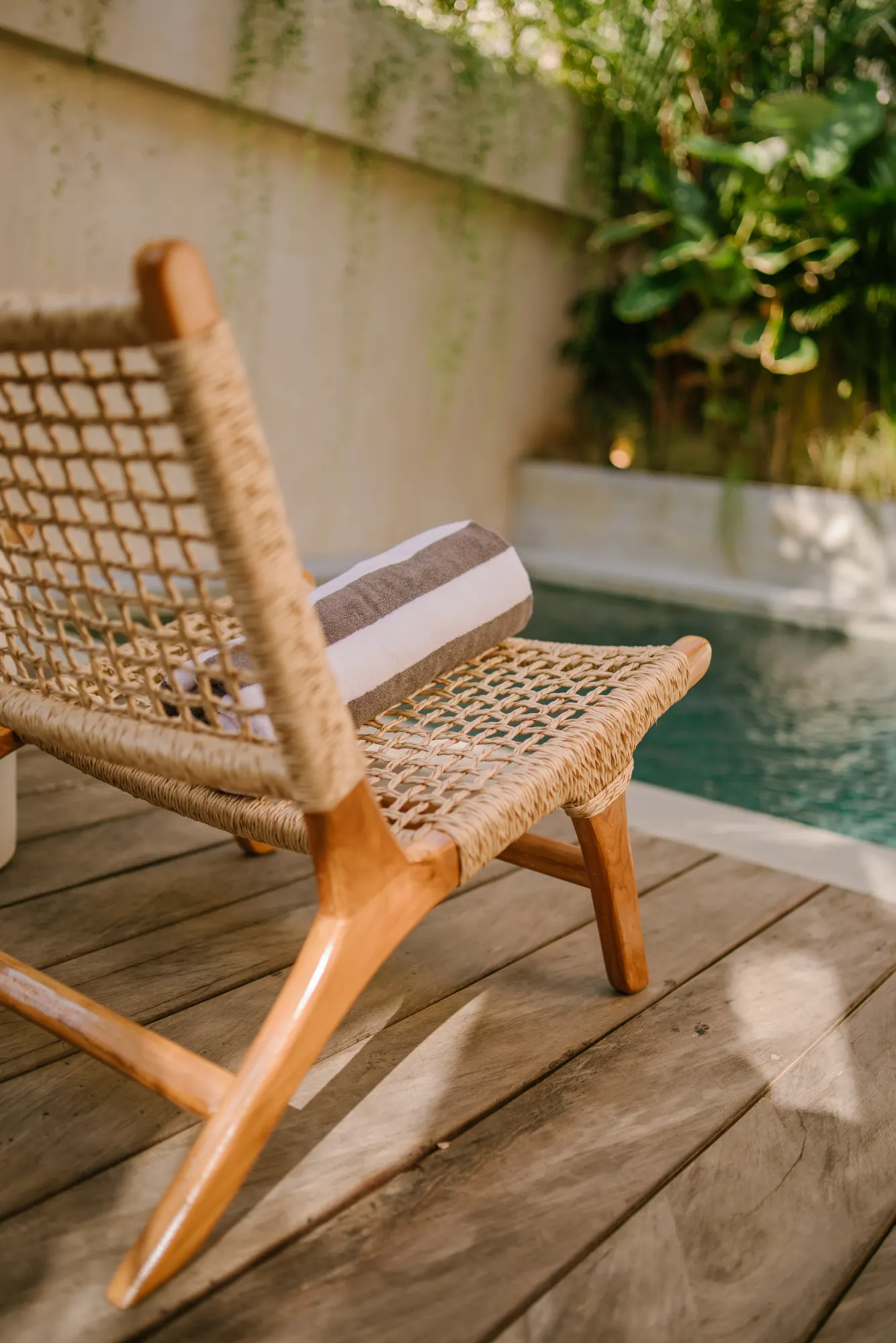 Woven lounge chair on pool deck with lush garden backdrop